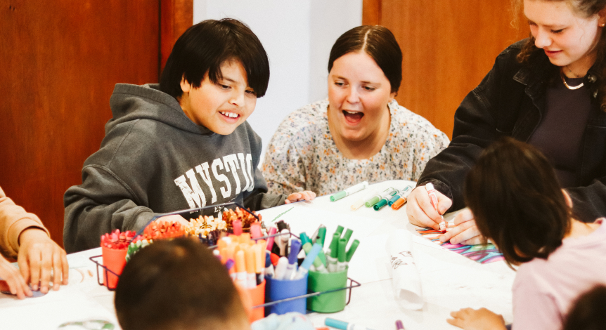 College student sitting at desk tutoring young children